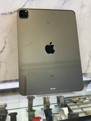 An Apple iPad with a dark metallic gray back panel, standing upright on a glass display stand in front of a white marble-patterned wall.