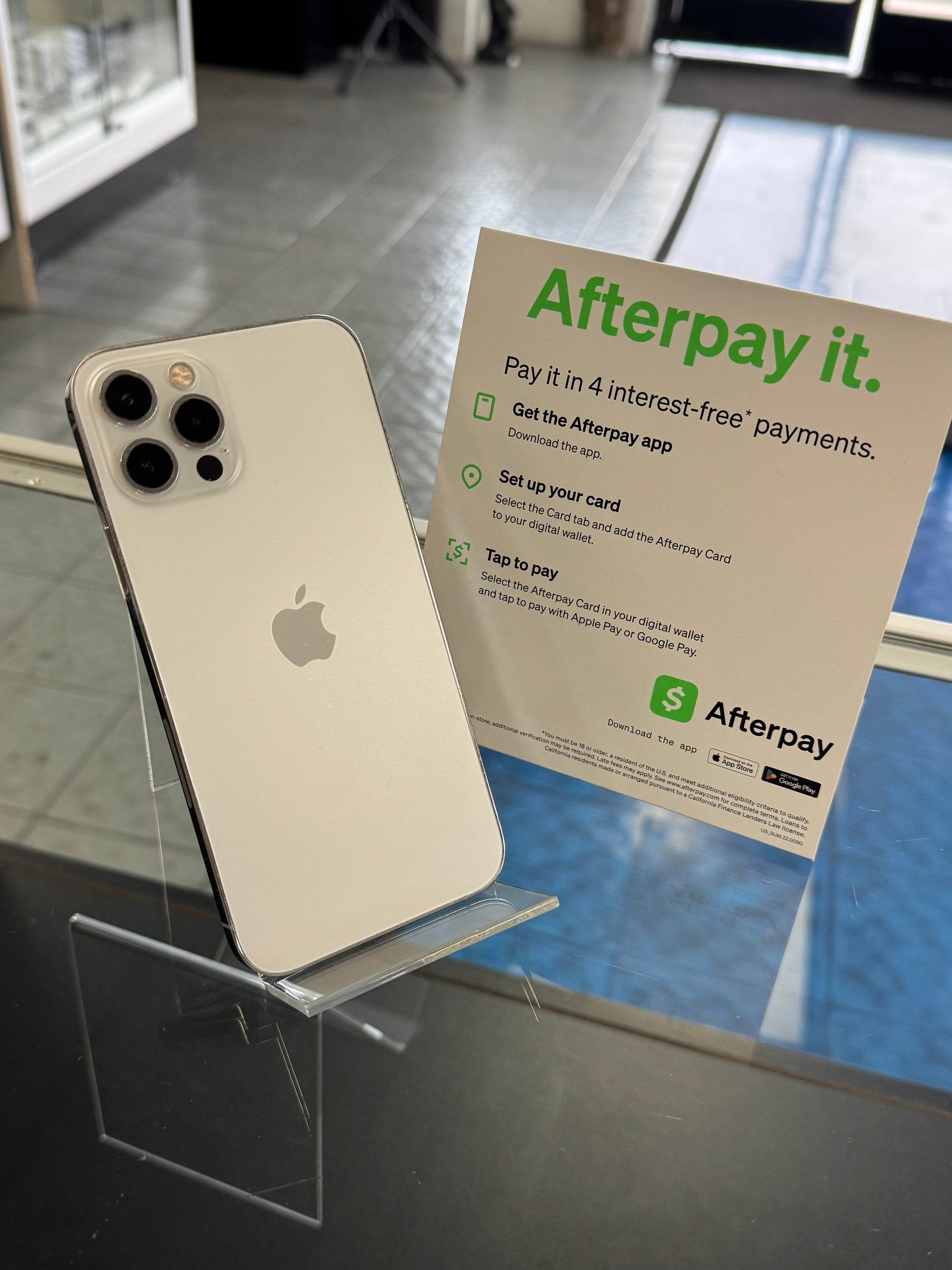 Apple smartphone on a stand with an Afterpay promotional sign in the background