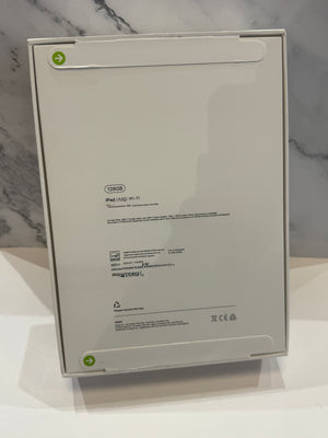 The back of a white Apple iPad box, showing product specifications and regulatory text, set against a gray marble-patterned background.
