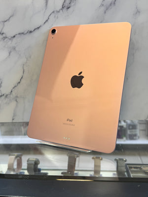An Apple iPad with a rose gold aluminum back, displayed on a clear stand against a white marble background.
