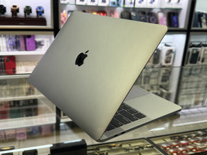 A silver Apple MacBook laptop with its lid open, resting on a glass display counter inside a retail store. The Apple logo is clearly visible on the back of the laptop lid.