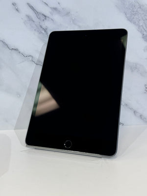 A black Apple iPad tablet with a glossy screen, standing upright on a clear plastic display stand against a white marble-patterned background.
