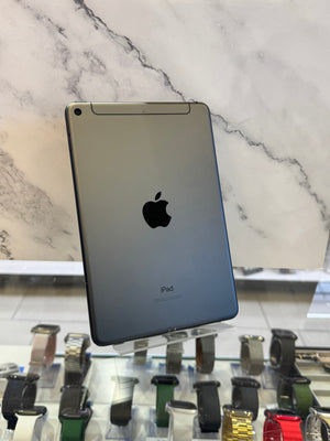 A silver Apple iPad Pro shown from the back, standing on a clear display stand in a retail setting with a marble-patterned wall behind it and multiple smartwatches visible on a counter below.