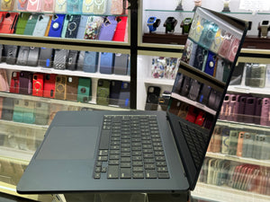 Laptop displaying phone cases on screen with shelves of phone cases in the background