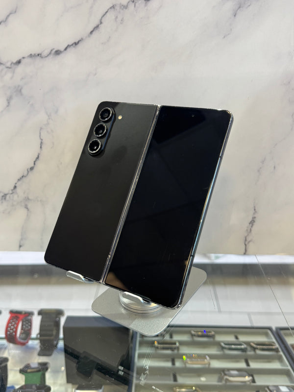 A black Samsung Galaxy S24 Ultra smartphone shown open in a foldable mode, displayed on a stand in front of a marble-patterned wall.