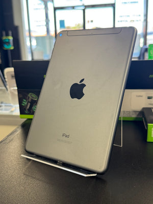 A silver Apple iPad shown from the back, standing on a clear display stand on a dark tabletop in a store setting.