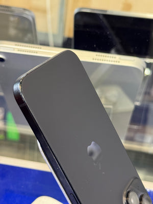 A close-up of the back of a black Apple iPhone, showing the glossy black finish, the silver Apple logo, and part of the camera module, resting on a reflective glass surface.