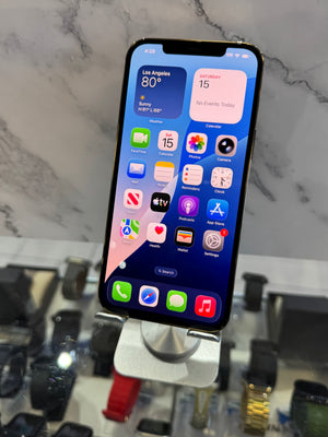 A black smartphone displayed upright on a stand in a retail setting, with a marble-patterned background and other watches or accessories blurred below.