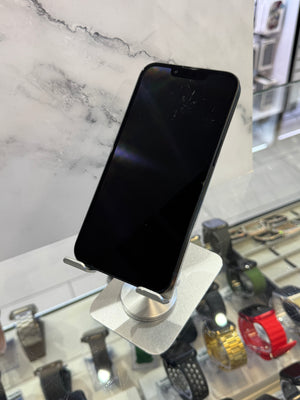 A black smartphone with a screen protector display, resting on a silver metal stand in a retail store setting with watch displays in the background.