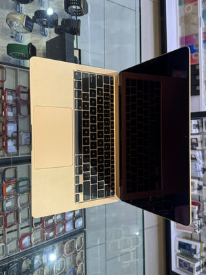 An Apple MacBook laptop with a black keyboard and screen, shown open on a glass display counter in a retail store.