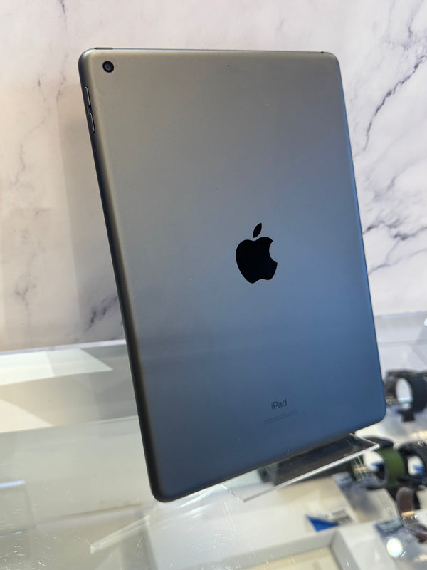 A silver Apple iPad standing upright on a glass display stand, showing the back of the device with the Apple logo and 'iPad' text, set against a marble-patterned background.