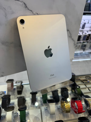 An Apple iPad with a silver aluminum back, resting on a white marble surface with a blurred watch display in the background.