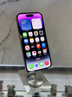 A black smartphone with a lit home screen displaying colorful app icons, resting on a metallic silver display stand against a light gray marble-patterned background.