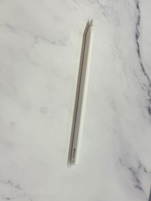 A white Apple Pencil with a silver tip lies diagonally on a white marble surface.