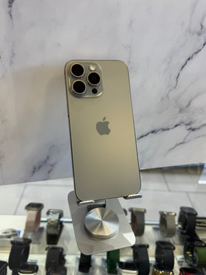 An Apple iPhone in a light metallic gray color, shown from the back, resting on a white marble-patterned surface next to a display stand with other watches.