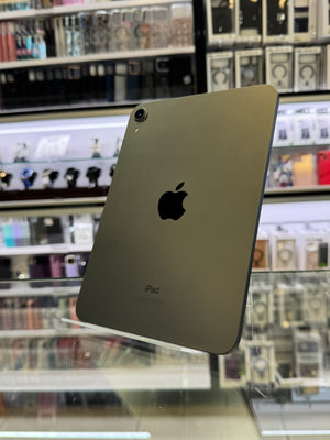 A grey-colored iPad shown from the back, resting on a glass display counter inside a retail store with shelves of accessories in the background.