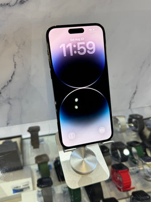A black smartphone with a large front-facing camera cutout stands on a silver display stand inside a watch store. The screen is on and displays a blue-to-purple gradient lock screen.