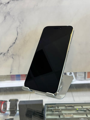 A silver smartphone with a black screen stands on a clear display stand inside what appears to be a retail store, with a marble-patterned wall behind it.
