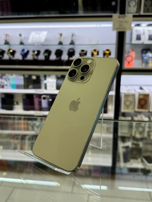 An Apple iPhone Pro displayed on a clear acrylic stand inside a retail store, with blurred shelves of accessories in the background.
