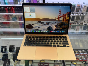 A gold Apple MacBook laptop with a black keyboard and trackpad, displaying the San Francisco skyline on its screen, set against a blurred retail background.