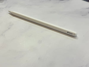A white Apple Pencil resting diagonally on a white marble surface, with the Apple logo and 'Pencil' text visible near the tip.