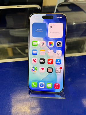 A black iPhone with its screen turned on, displaying the home screen and widgets, resting on a clear plastic stand against a blue surface.