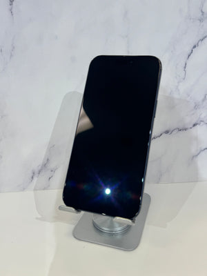 A black smartphone with a blank screen stands upright on a clear acrylic display stand against a white marble-patterned background.