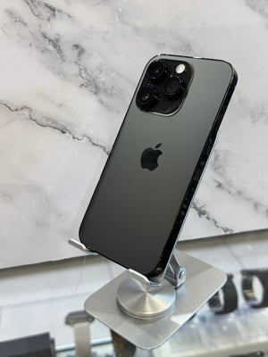 A black Apple iPhone 12 Pro shown from the back, resting on a silver metal display stand against a white and gray marble-patterned background.