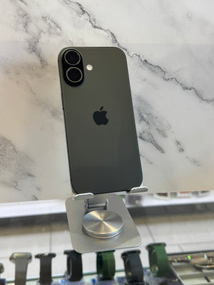 A dark gray Apple iPhone with a black camera bar, standing upright on a silver metal stand against a white marble-patterned background.