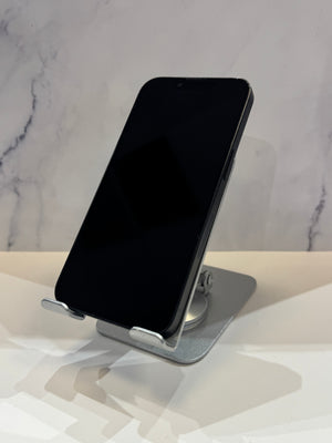 A black smartphone displayed upright on a silver metal stand against a light marble-patterned background.