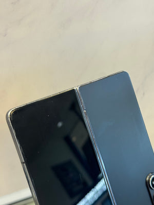 Close-up of a black foldable smartphone showing the hinge and outer screen panel against a light marble-like background.