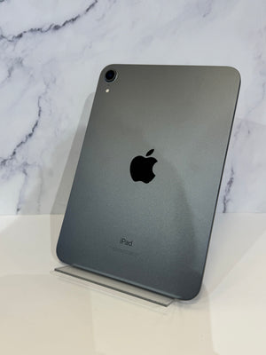 A dark gray Apple iPad standing upright on a clear acrylic display stand against a white marble-patterned background.