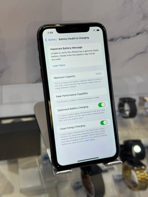 A black smartphone displaying the Battery Health & Charging settings screen, resting on a clear display stand in a retail or showroom setting.