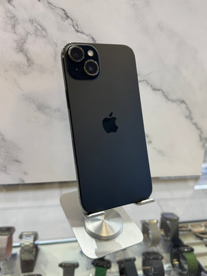 A black Apple iPhone 12 Pro shown from the back, resting on a white and gray marble display stand in a retail setting.
