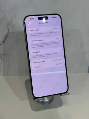 A black smartphone displayed upright on a silver stand, showing the battery health screen on the home screen. The phone is photographed against a light marble-patterned background.