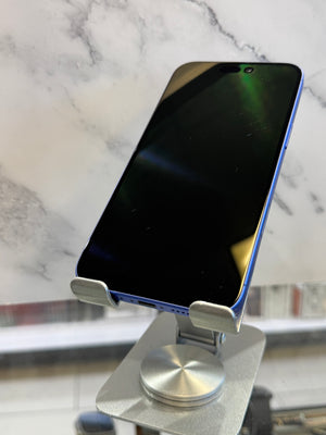 A smartphone with a black screen and blue edges displayed on a silver metal stand, set against a white marble-patterned background.