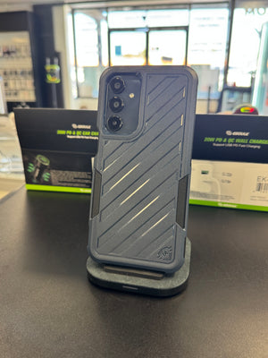 A dark gray rugged smartphone case with diagonal textured stripes, shown on a charging stand on a dark tabletop. Two black and green Govee product boxes are visible in the blurred background of what appears to be a retail store.