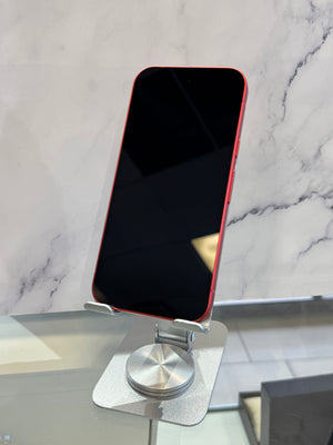 A red smartphone with a black screen stands upright on a silver metal display stand against a white marble-patterned wall.