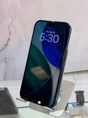 A black smartphone with a dark blue and green lock screen wallpaper, standing on a silver metal display stand.