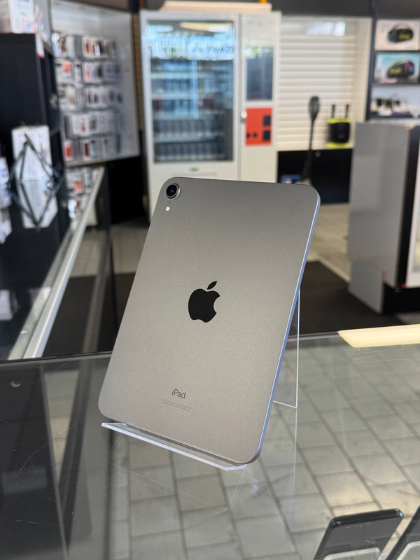 A silver Apple iPad shown from the back, standing on a clear display stand on a glass counter inside a retail store.