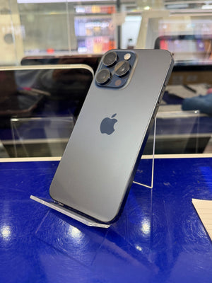 A dark gray Apple iPhone Pro showing the back of the device with its triple-camera system and Apple logo, displayed on a clear stand on a blue counter in a store setting.