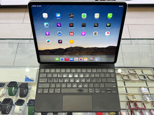 A dark gray Apple Magic Keyboard with a Touch ID sensor, attached to an iPad with a colorful home screen, displayed on a glass counter in a retail store.