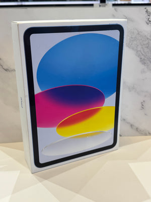 A white Apple iPad box standing upright on a light surface, with the front showing the iPad screen and colorful abstract wallpaper. The background is a marble-patterned wall.