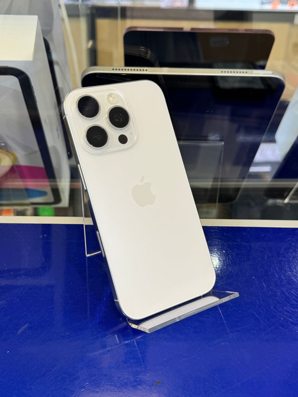 A white Apple iPhone 12 Pro shown from the back, resting on a small clear display stand against a bright blue wall in a retail or showroom setting.