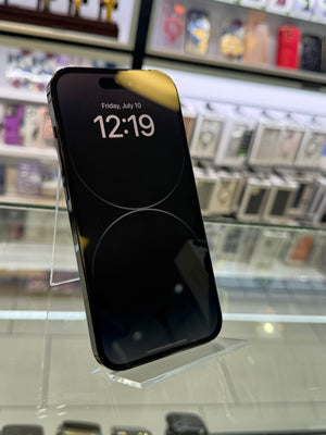 A black smartphone with a lit lock screen displaying the time 12:19, standing on a clear acrylic display stand inside a retail store with blurred shelves in the background.