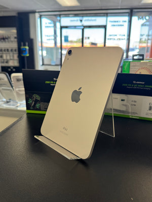 An Apple iPad with a light finish, shown from the back resting on a clear acrylic stand on a dark counter inside a retail store.