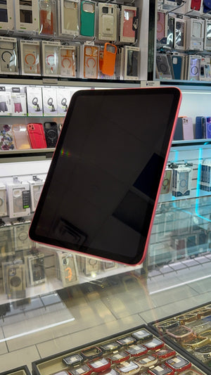 A tablet with a black screen and a pinkish-red protective case, shown at an angle inside a retail store display case with other accessories in the background.