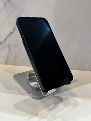 A black smartphone displayed upright on a silver metal stand against a light marble-patterned background.