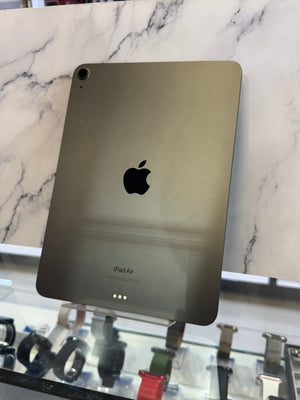 An Apple iPad Air in matte dark gray or charcoal color, shown from the back with the Apple logo visible, displayed on a stand in front of a marble-patterned background.