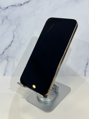 A black smartphone with a gold-toned edge rests on a silver metal stand against a white marble-patterned background.
